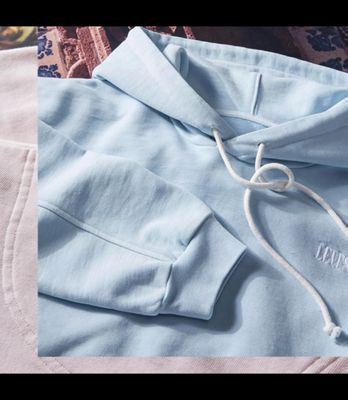 Man wearing a light blue hoodie standing in front of a mosaic background.