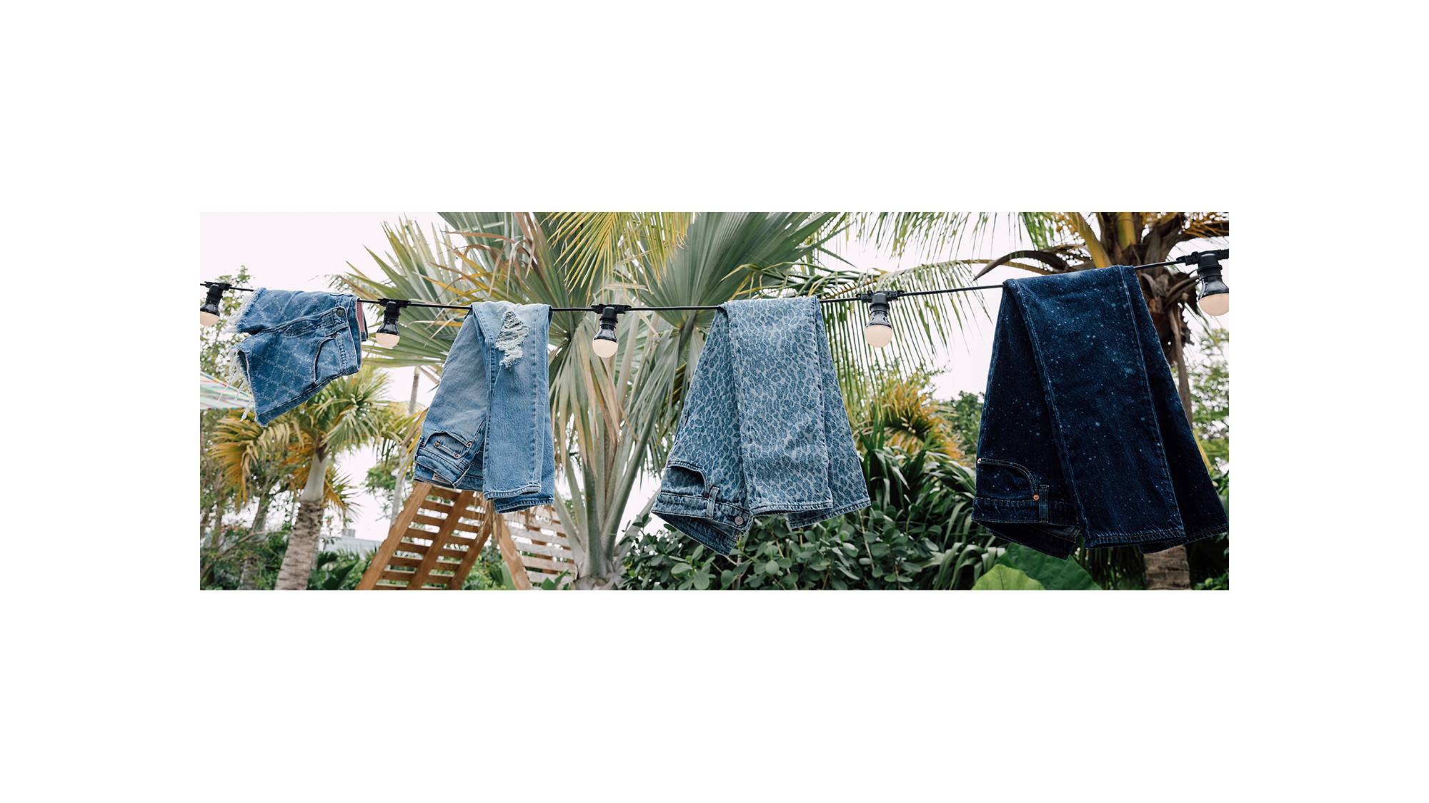 Image of four pairs of Levi's® jeans created by the Future Finish process hanging on a line of string lights with palm trees in the background.