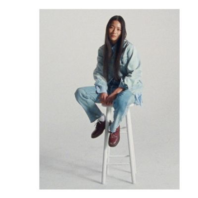 A photo of Yulu Serao sitting on a white stool, looking at the camera wearing an oversized Levi's Trucker jacket and Levi's jeans