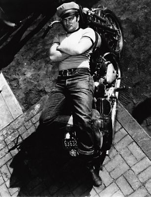 A black and white photo of Marlon Brando wearing 501 jeans lying on a motorcycle.