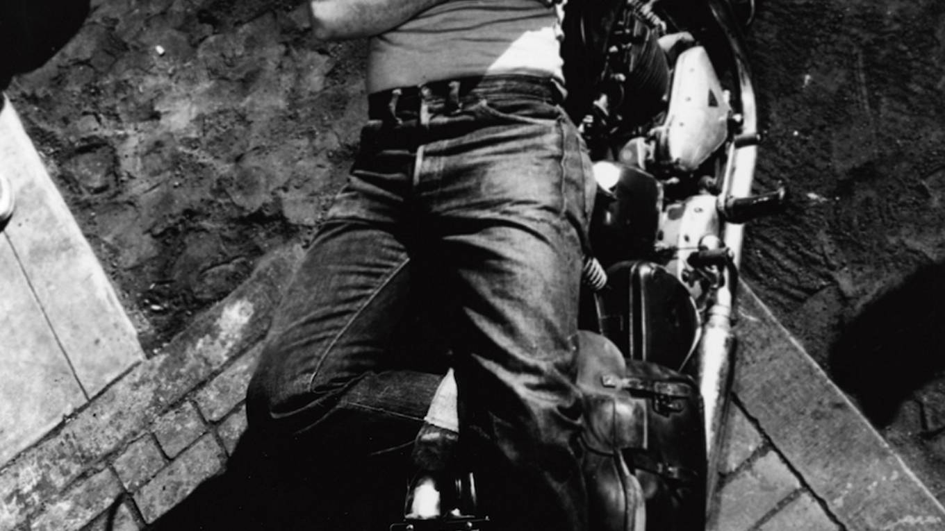 A black and white photo of Marlon Brando wearing 501 jeans lying on a motorcycle.
