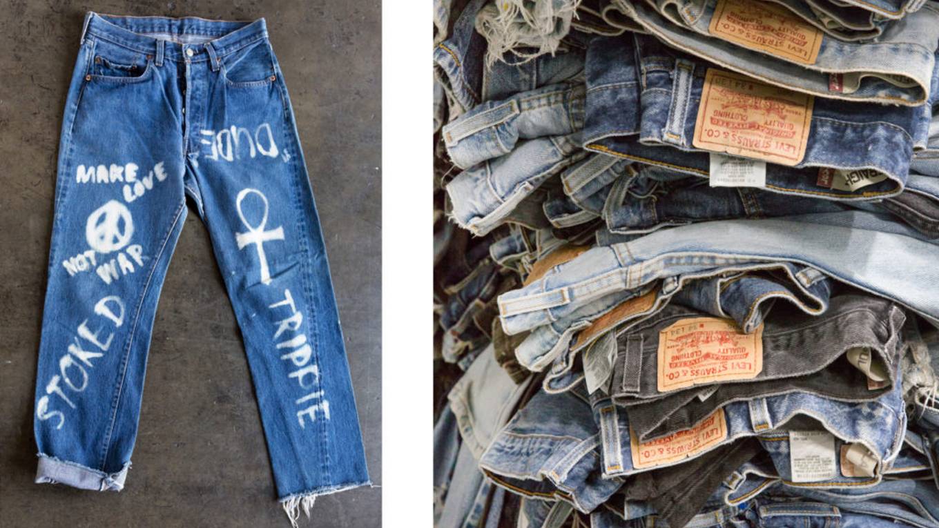 Jeans laying flat on the floor and having white spray paint with words on them.