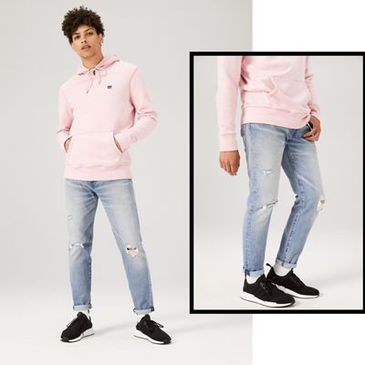 Man wearing a pink hoodie and modeling the Hi-Ball Roll jeans.