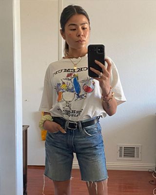 Mirror selfie of Katya Linehan. She is wearing a white graphic tee and cut-off Levi's.