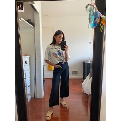 Mirror selfie of Katya Linehan. She is wearing a white graphic tee and flared Levi's bottoms with yellow platform sandals.