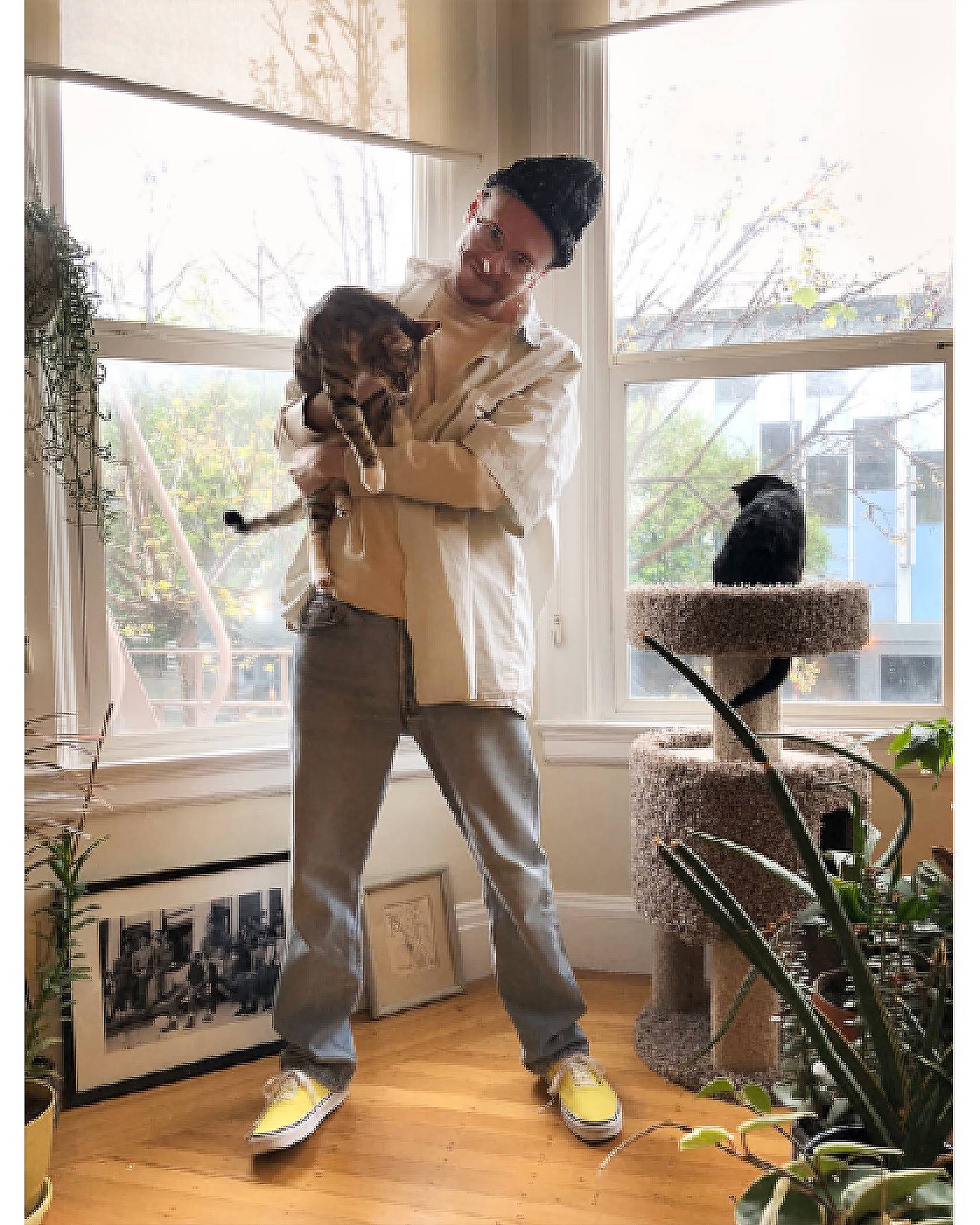 Photo of Ezra Price in his apartment. He's holding his cat and smiling.