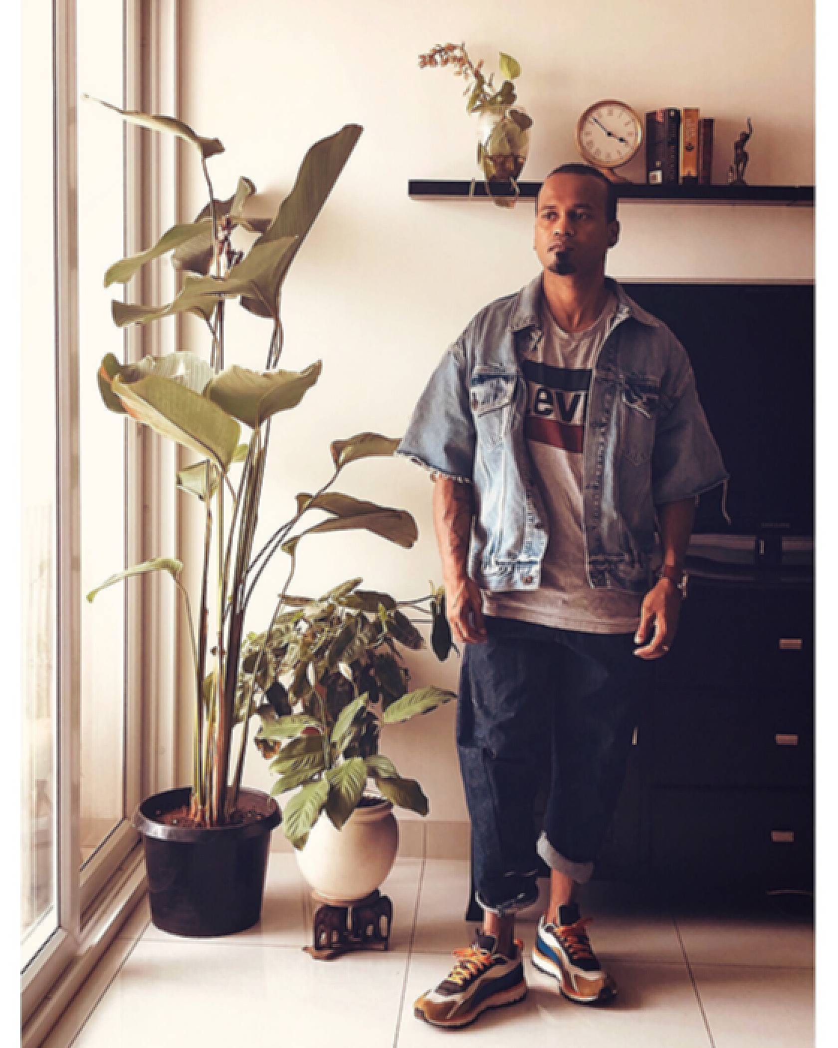 Photo of Ramu Mohan standing by a window inside his home. He is wearing a Levi's logo tee, a Levi's Trucker Jacket with cut-off, frayed sleeves, cuffed jeans, and chunky, colorful sneakers.