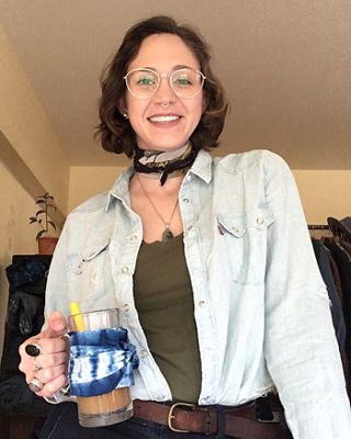 Image of Levi's® tailor Jen Sharkey wearing a light wash denim western shirt, printed bandana, and holding a glass mug filled with coffee, a yellow straw and blue bandana wrapped around it.