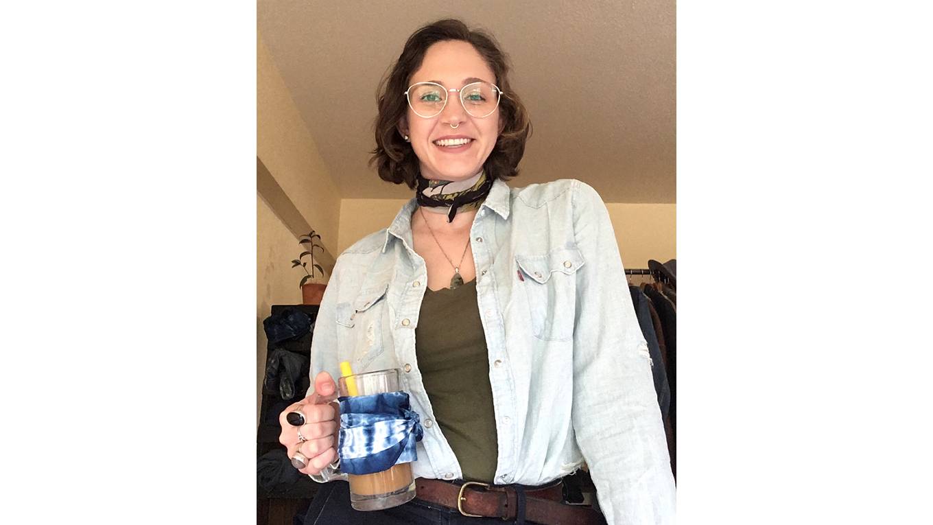 Image of Levi's® tailor Jen Sharkey wearing a light wash denim western shirt, printed bandana, and holding a glass mug filled with coffee, a yellow straw and blue bandana wrapped around it.