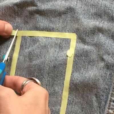 Video of tailor creating a freestyle geometric design with thin yellow tape on a light wash denim trucker jacket.