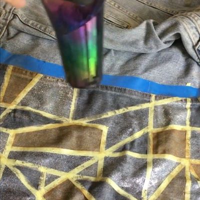 Image of a green and purple blowdryer to help speed up the process of glitter and gold paint to dry quicker on the back of a trucker jacket.