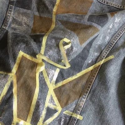 Video of thin yellow tape being removed from the back of a trucker jacket and the Levi's® tailor ironing the newly painted design with a layer of cloth to protect and lock in the design.