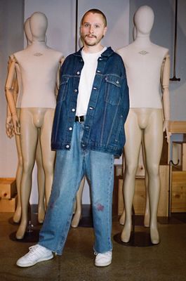 Photo of Ezra Price wearing a white tee with a dark indigo oversized Levi's Trucker Jacket and faded '90s style Levi's blue jeans and white sneakers.
