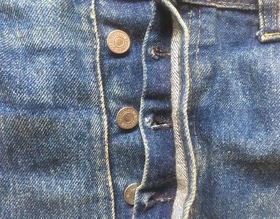 Close up image of the button fly on a pair of medium wash denim jeans.