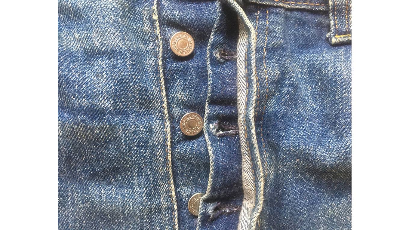 Close up image of the button fly on a pair of medium wash denim jeans.