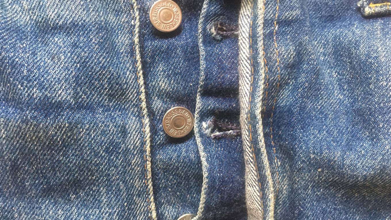 Close up image of the button fly on a pair of medium wash denim jeans.