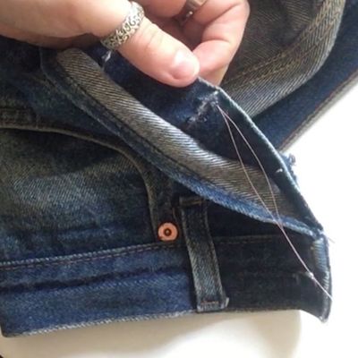 Image of secure a stitch's shape by looping several stitches around the hole where it was started on a pair of jeans.