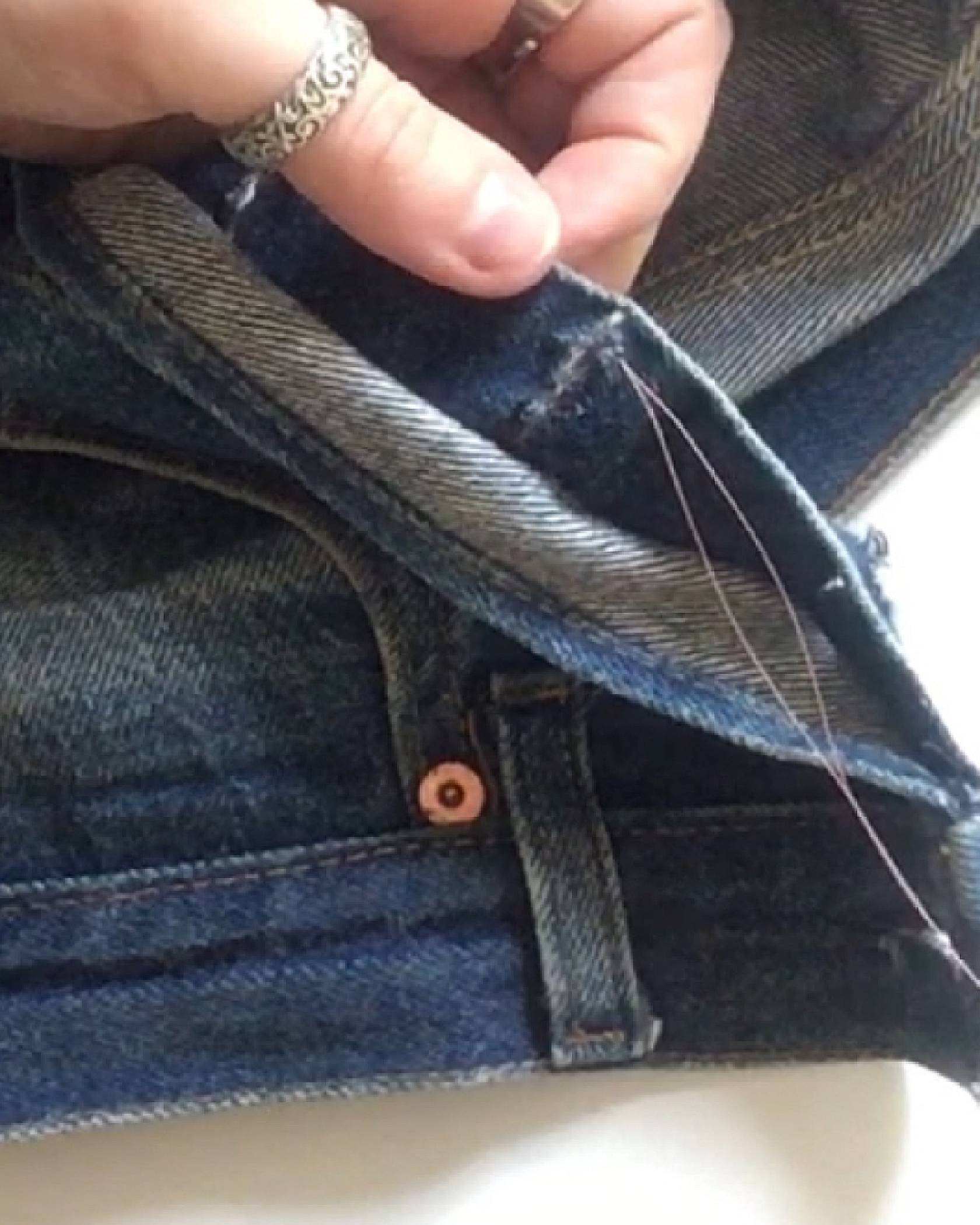 Image of secure a stitch's shape by looping several stitches around the hole where it was started on a pair of jeans.