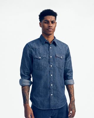 Marcus Rashford standing in a denim button up, not smiling.