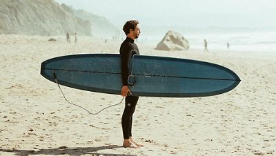 Rémi Sico debout portant sa planche de surf sous le bras