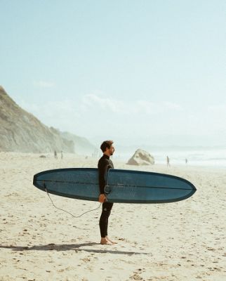 Rémi Sico debout portant sa planche de surf sous le bras