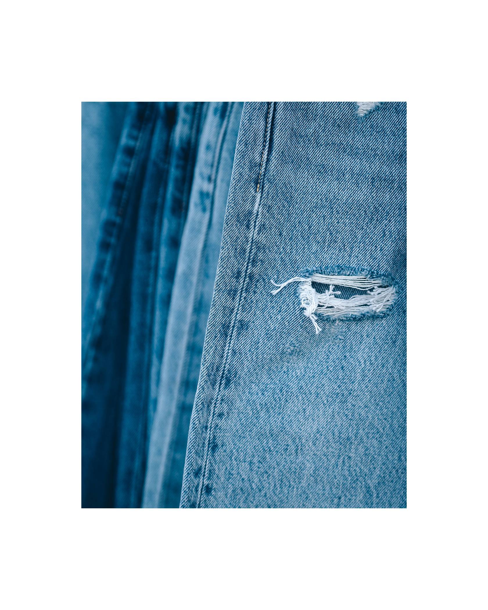 Imagery of a stack of blue denim jeans with a close-up shot of a rip on the pair of jeans closest to the camera.