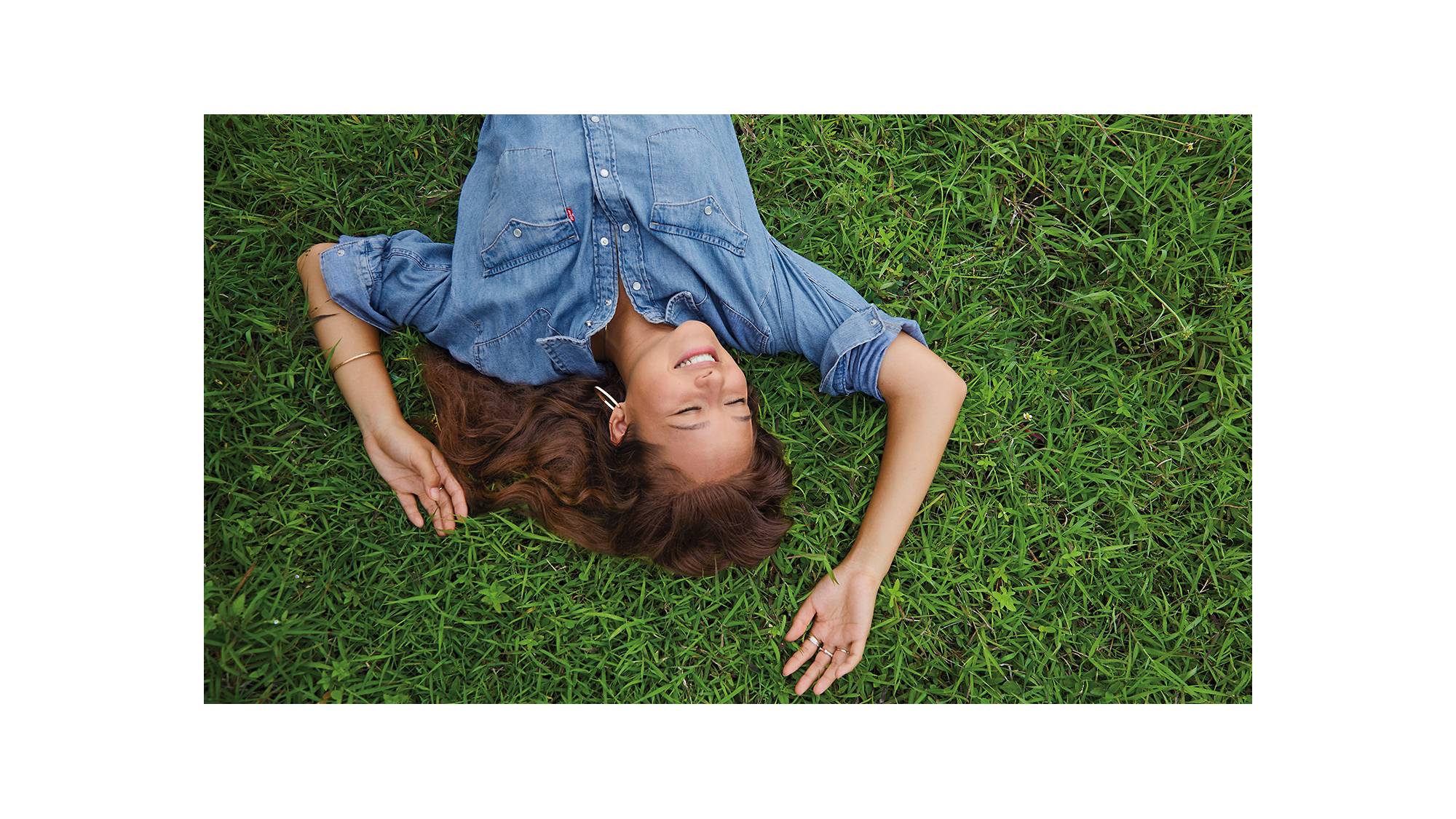A photo of Melati wearing a Levi's button up lying on green grass smiling
