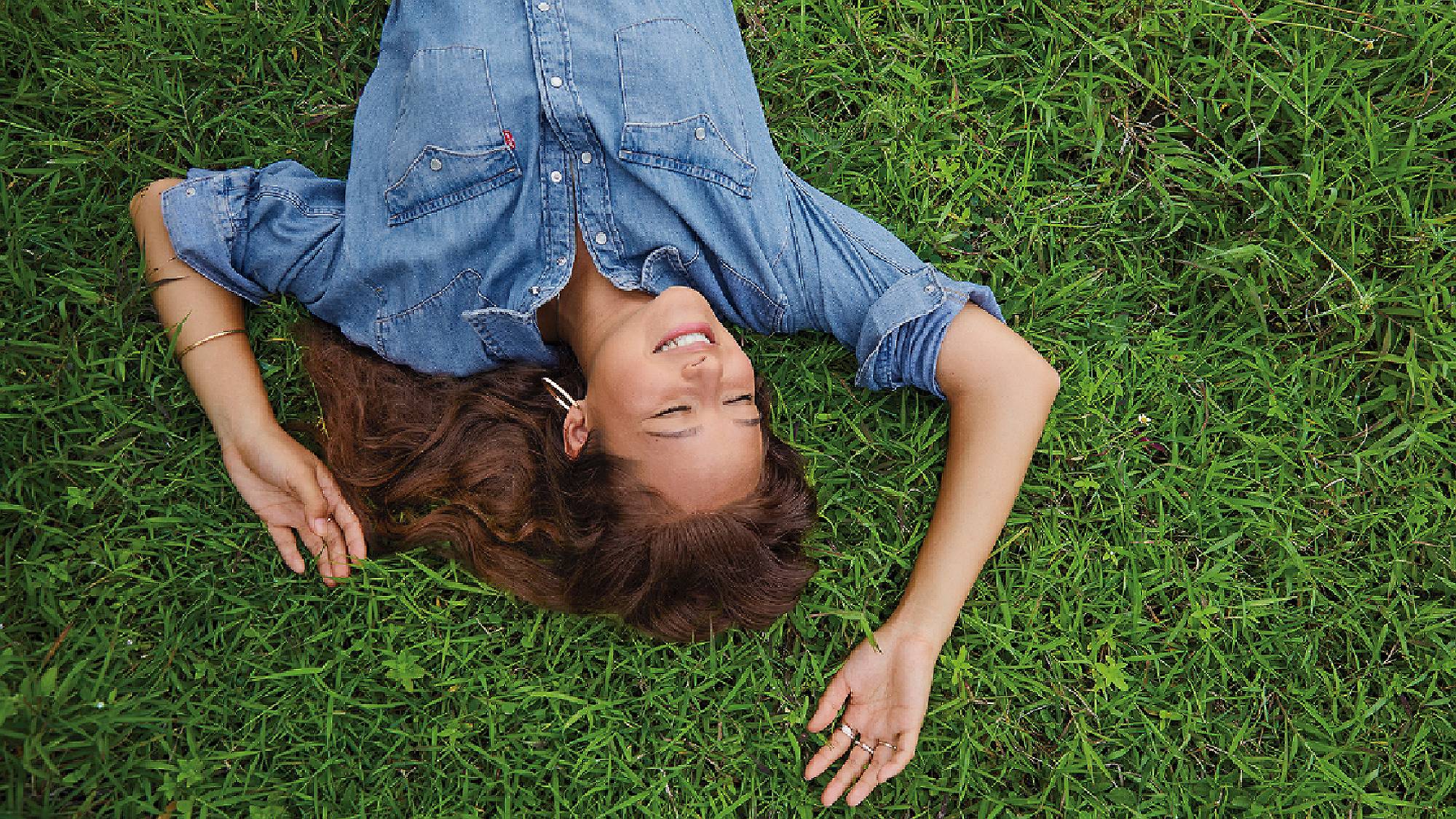A photo of Melati wearing a Levi's button up lying on green grass smiling