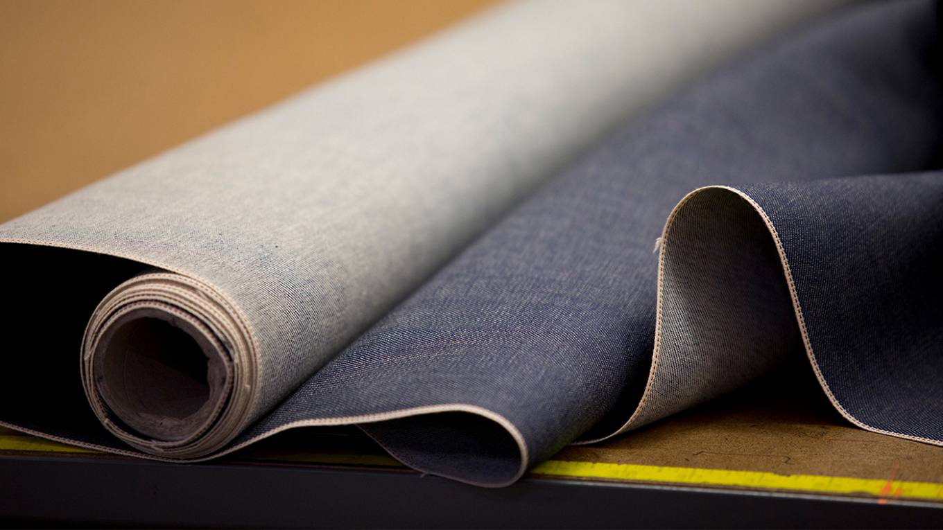 A fabric roll of denim rolled out on a table