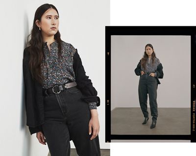 Woman wearing black high loose jeans and a black sweater, lounging against a wall.