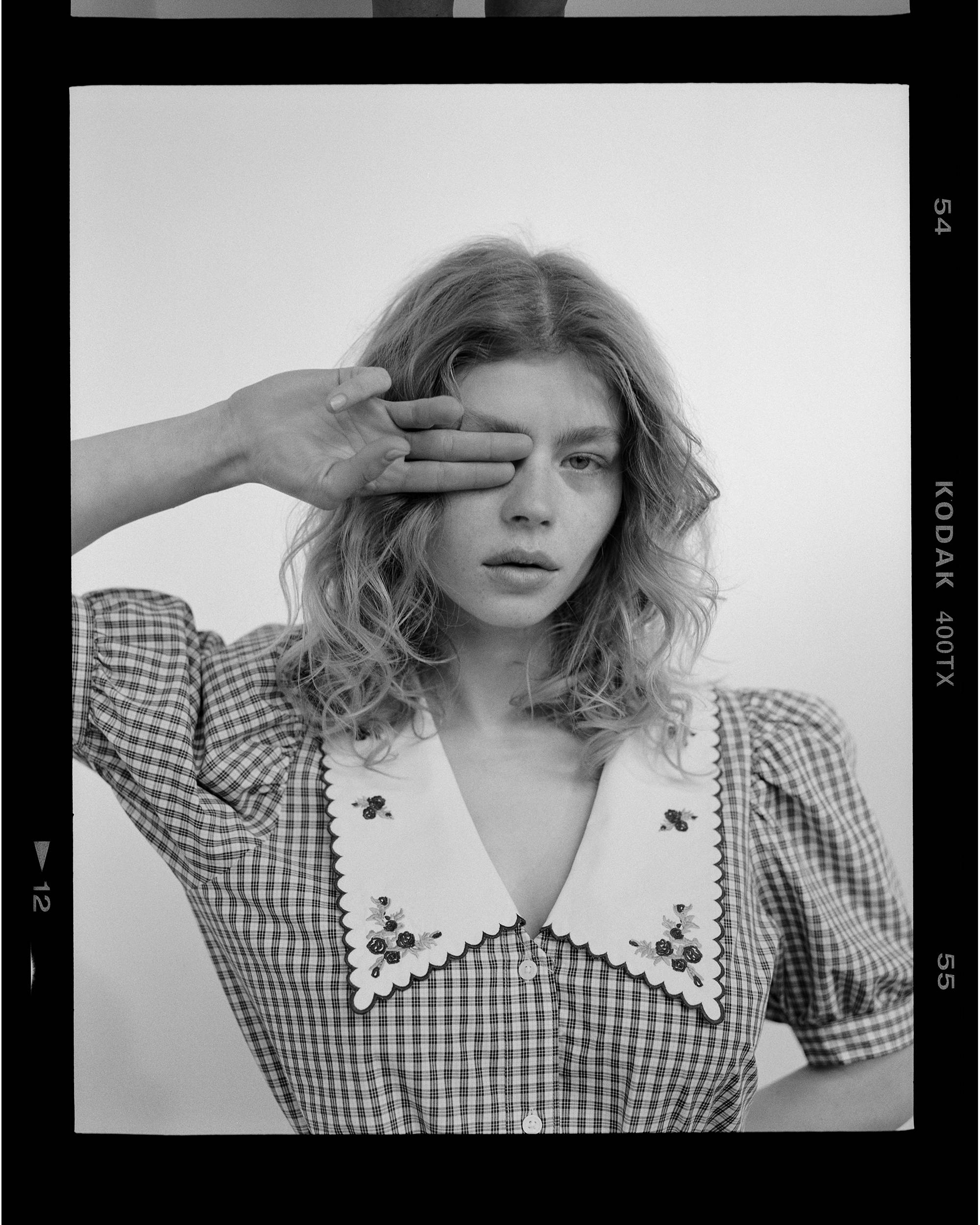 Black and white image with woman wearing a high button up with two fingers over her eyes.