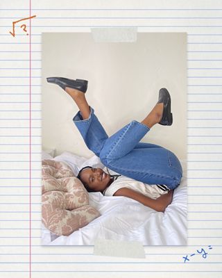 Image of woman wear math club jeans laying on bed kicking her legs up.