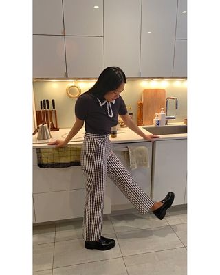 Image of woman wearing striped pants in the kitchen, looking at the floor and kicking up her leg.