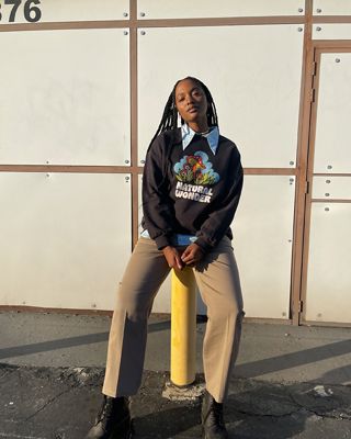 Image of woman sitting on a yellow pole and wearing khaki pants, posing.