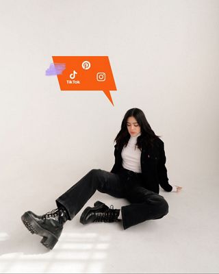 Luann sitting against a white backdrop wearing black jeans and matching Trucker with a white turtle neck with an illustrated thought bubble above her