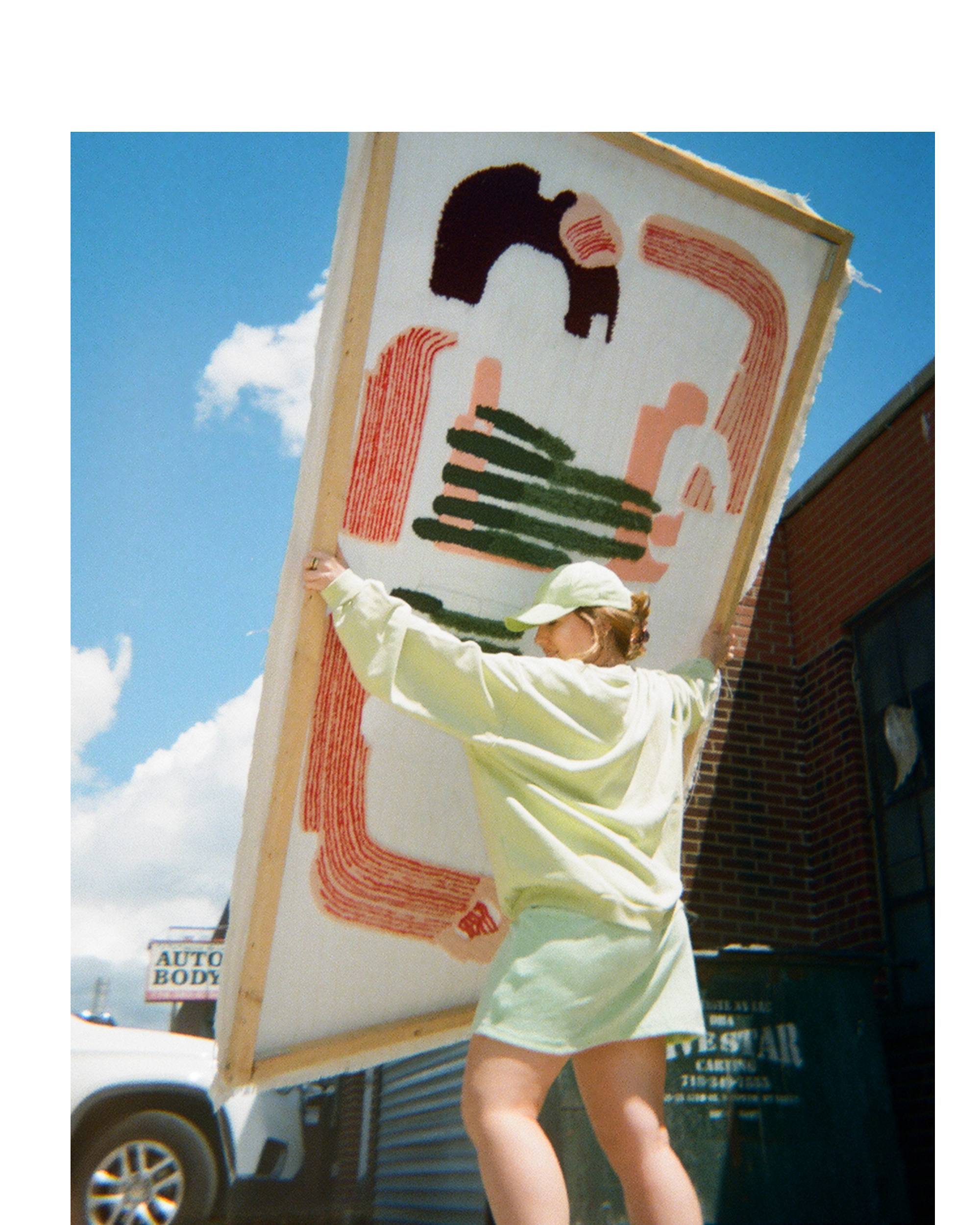 Caroline Kaufman wearing a levis outfit holding a large framed artwork