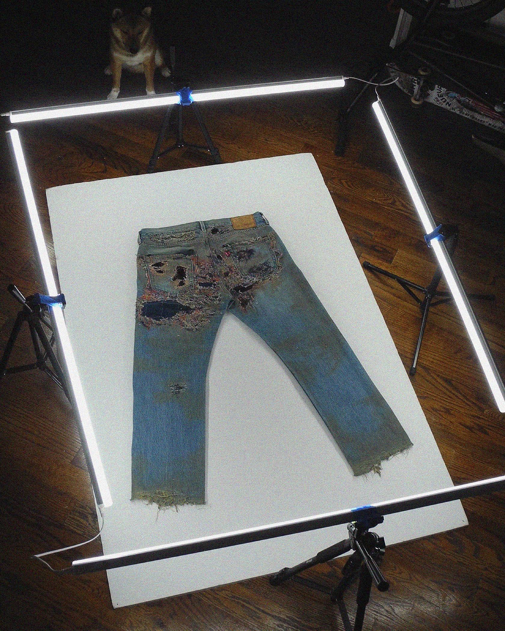 Phillip Leyesa's Levi's 501 Jeans after the customization process being photographed with studio lighting on a wooden floor.