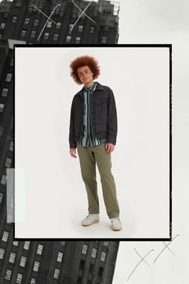 Model wearing black denim jacket, striped button down shirt, green chinos, and light gray shoes