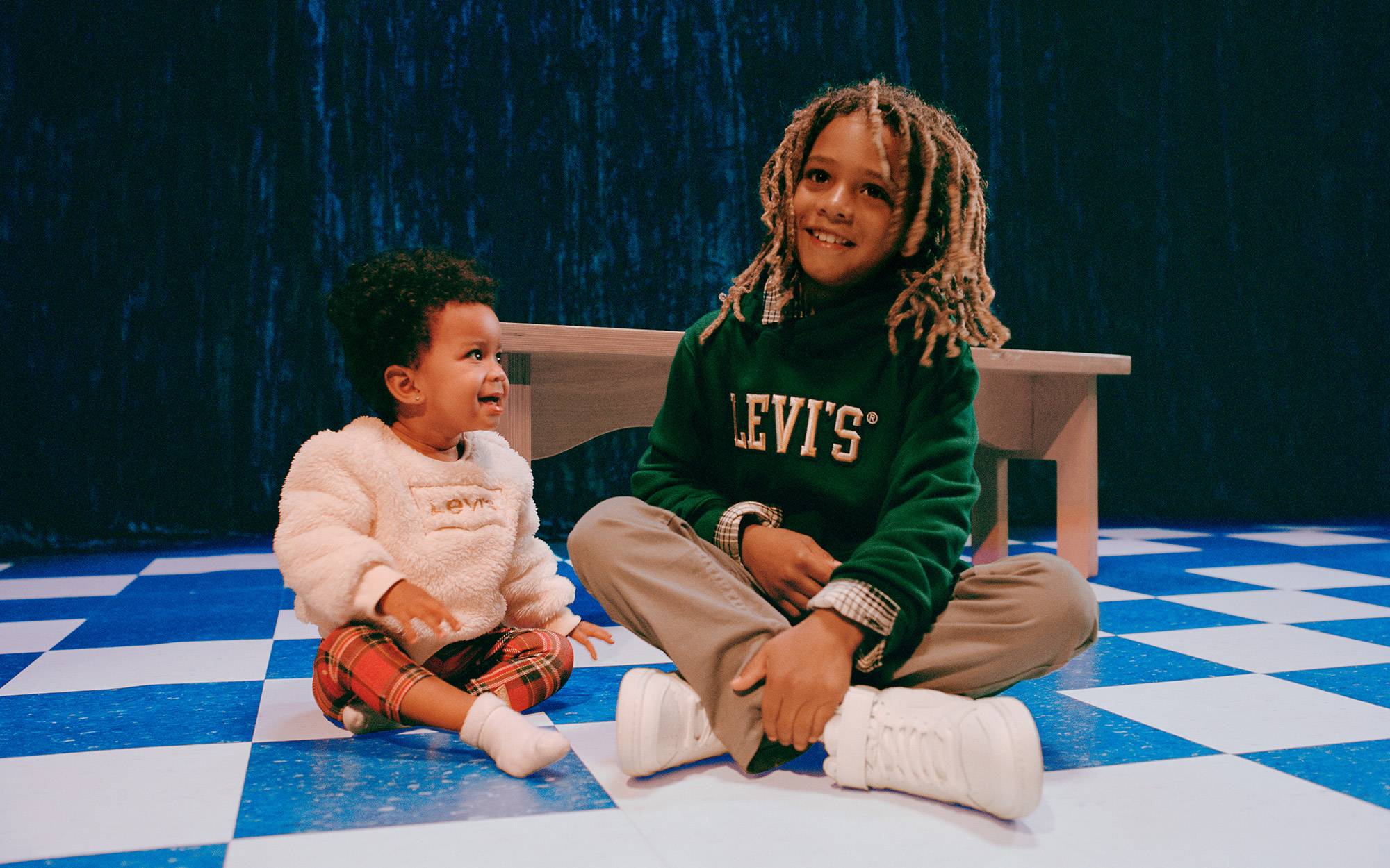 Two siblings (a baby and little boy) sitting on the floor together wearing Levi's seasonal product for the holiday.