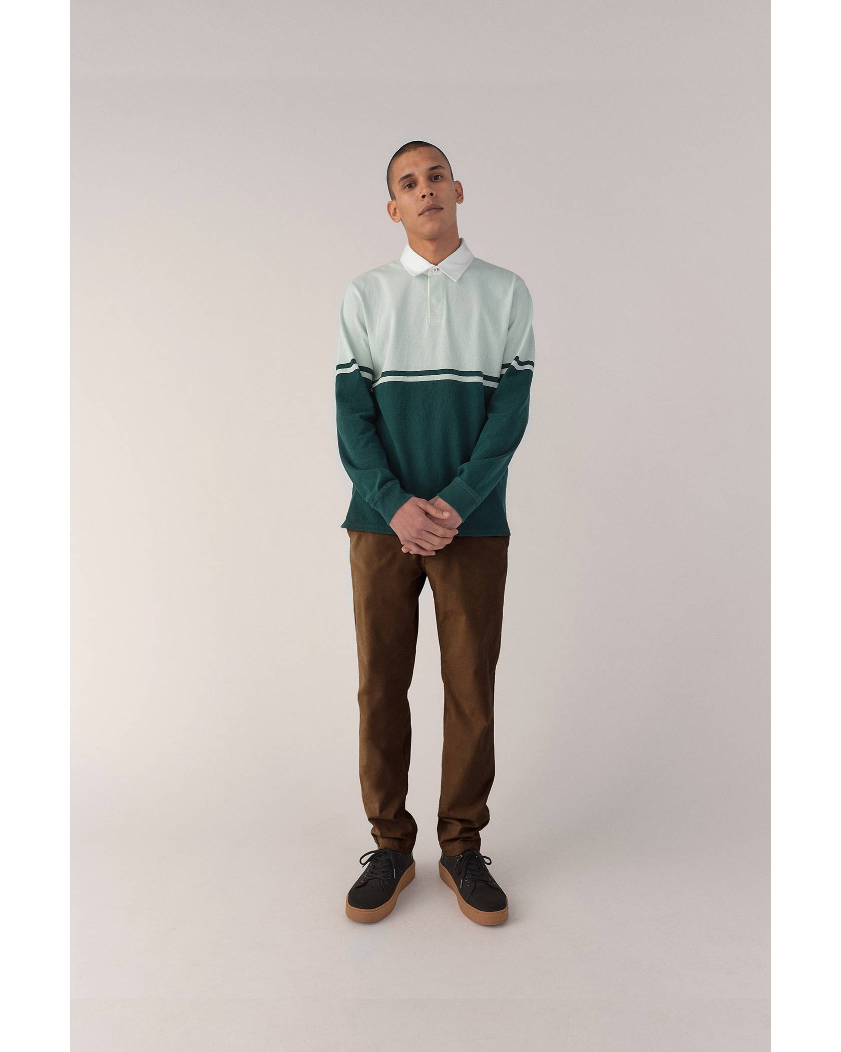 Model wearing mint and dark green collared shirt, brown pants, and black sneakers
