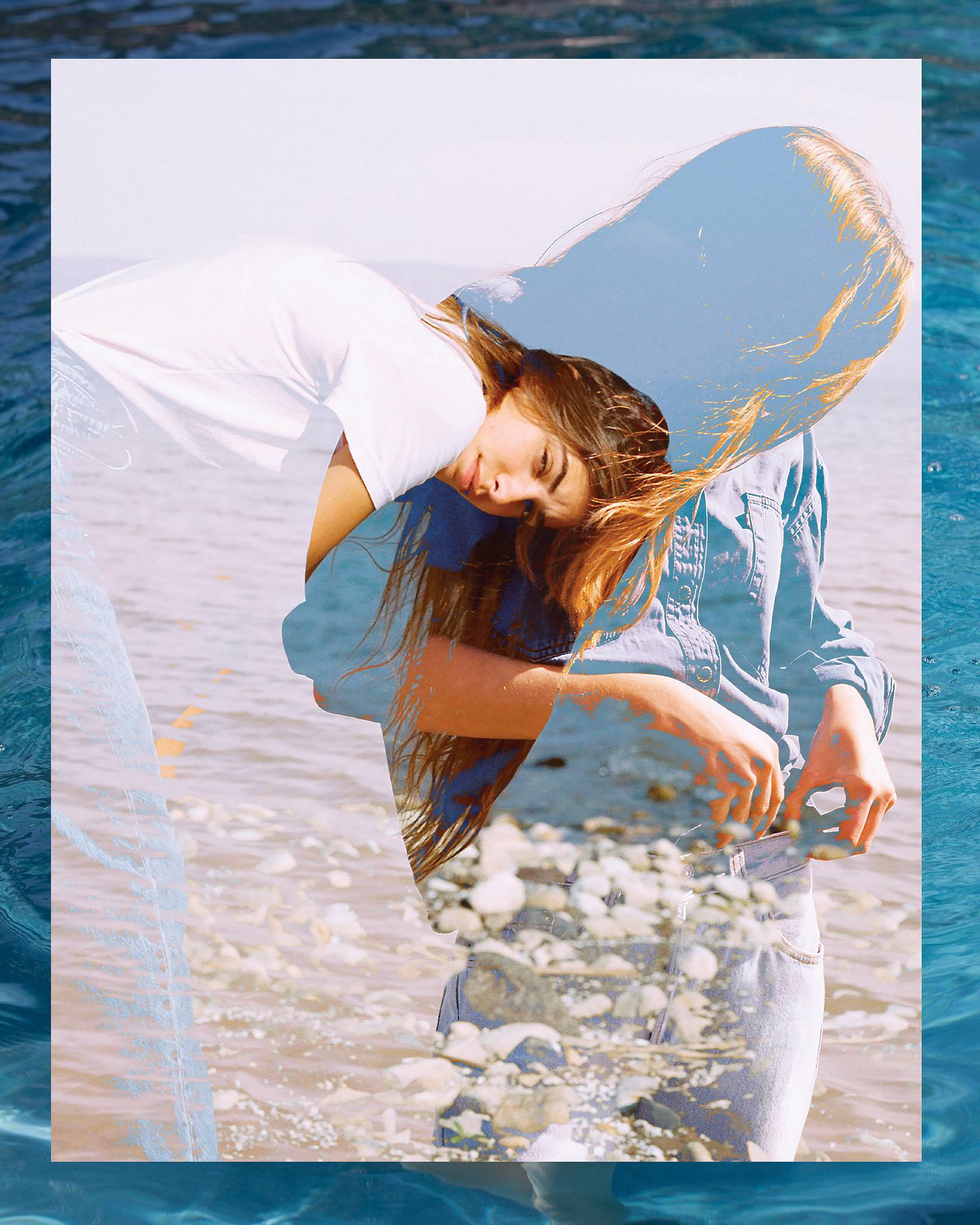 Women wearing a white tee and Levi's jeans standing in the ocean with her jeans cuffed up.