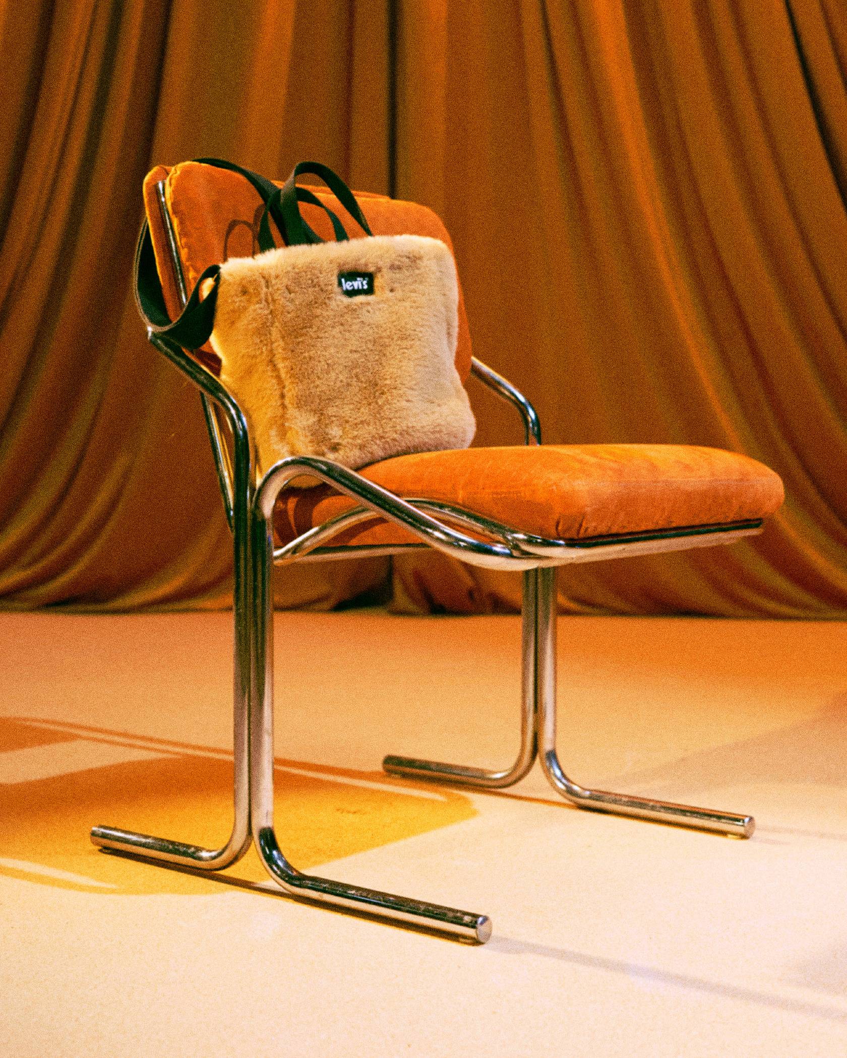 Fuzzy cream bag sitting on a mid century chair against a golden burnt orange backdrop