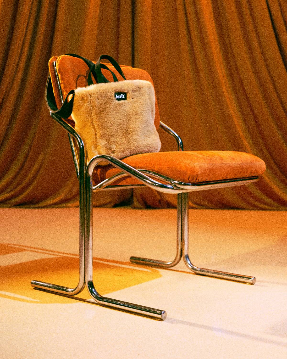 Fuzzy bag sitting on a mid century modern chair against a golden burnt orange backdrop