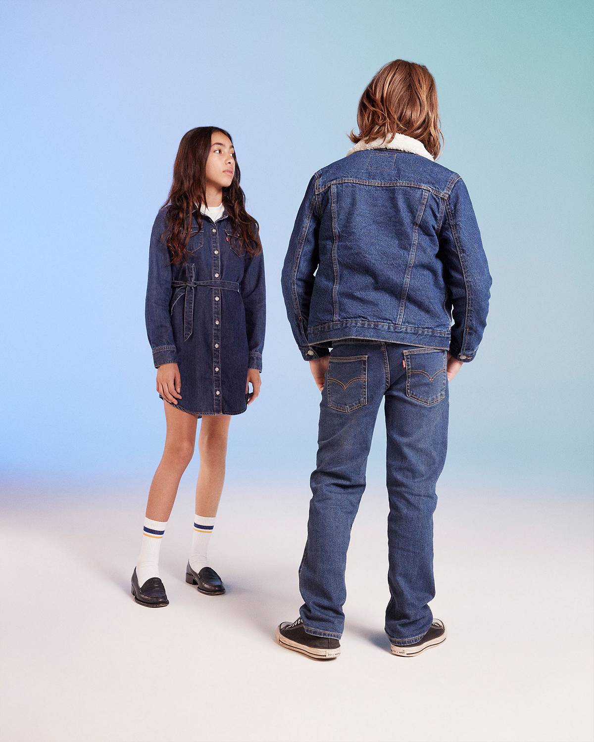 Models against a multi blue background in denim dress and all denim outfit