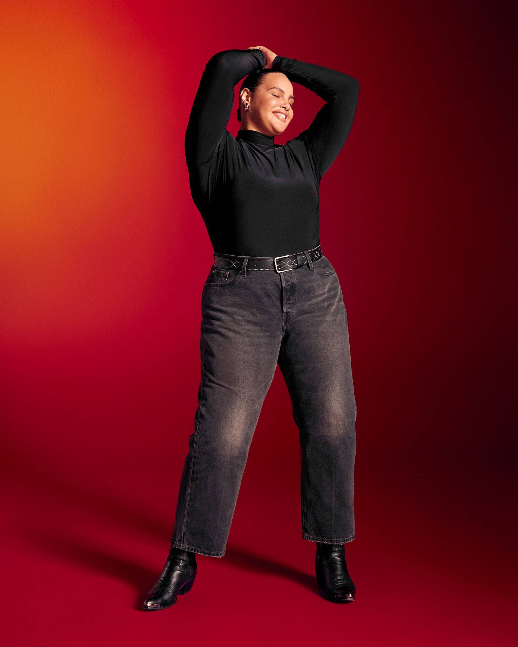 Model against a red background in black jeans and black mock neck long sleeve