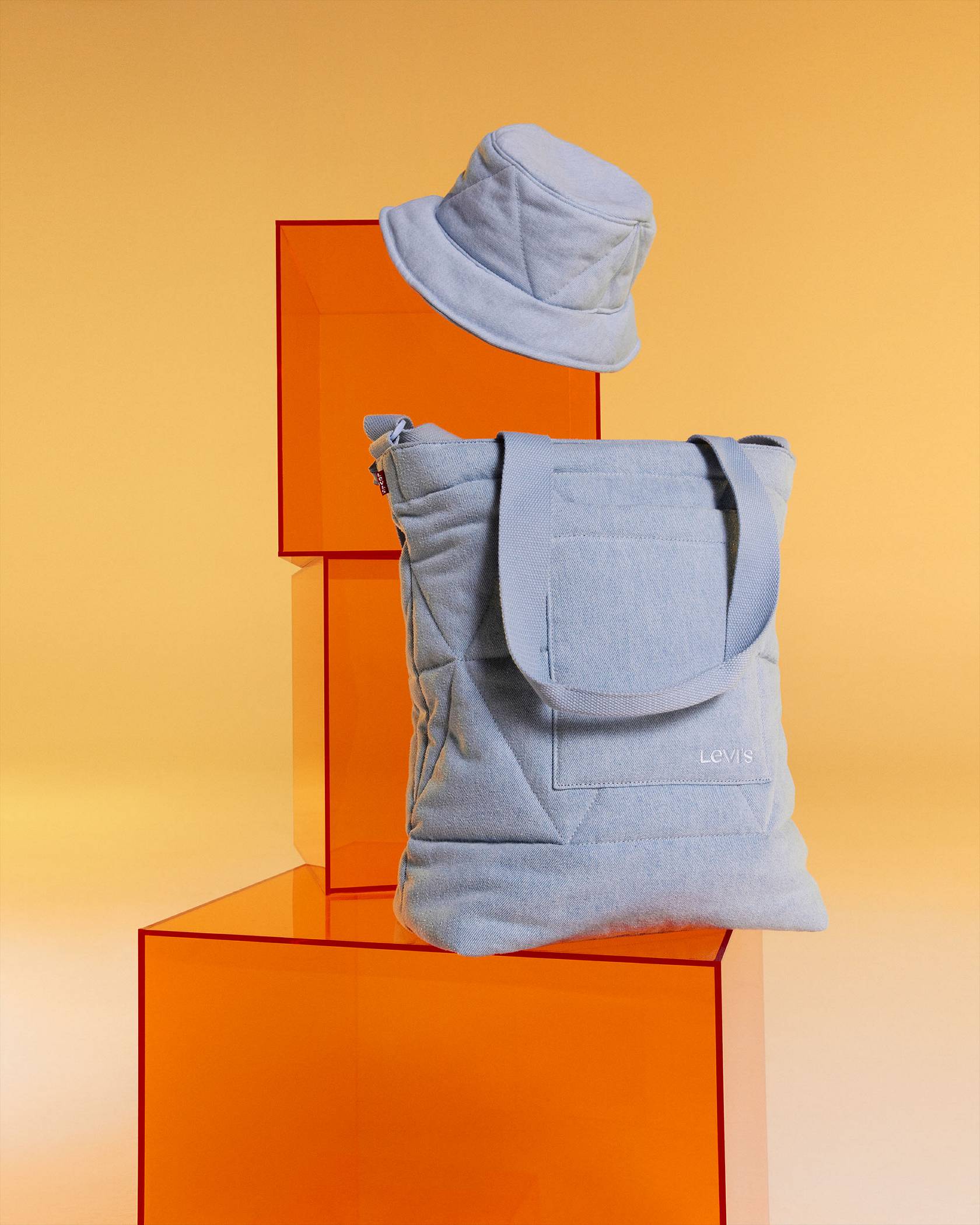 Denim accessories on orange acrylic boxes against a yellow background