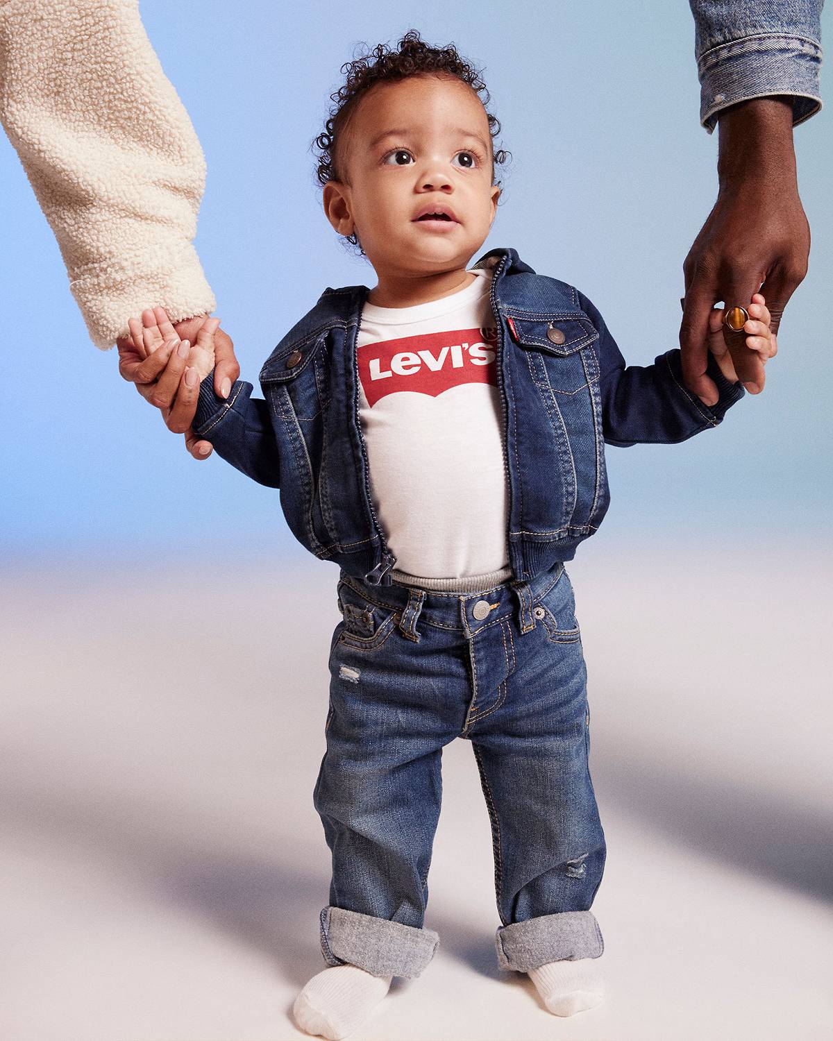 Model in toddler logo tee, jeans and trucker jacket against a blue background