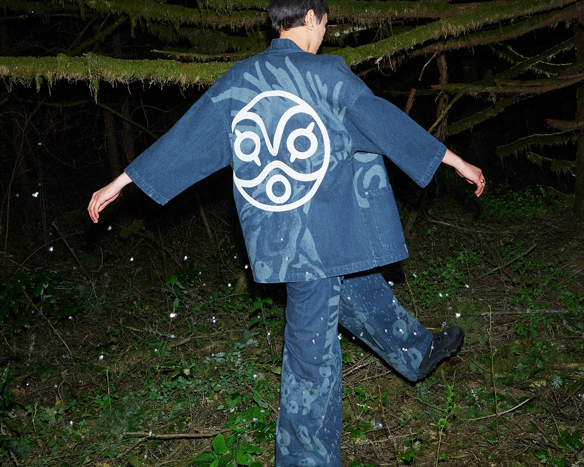 Image of woman wearing Levi's® x Princess Mononoke collection pieces and walking in nightime forest setting
