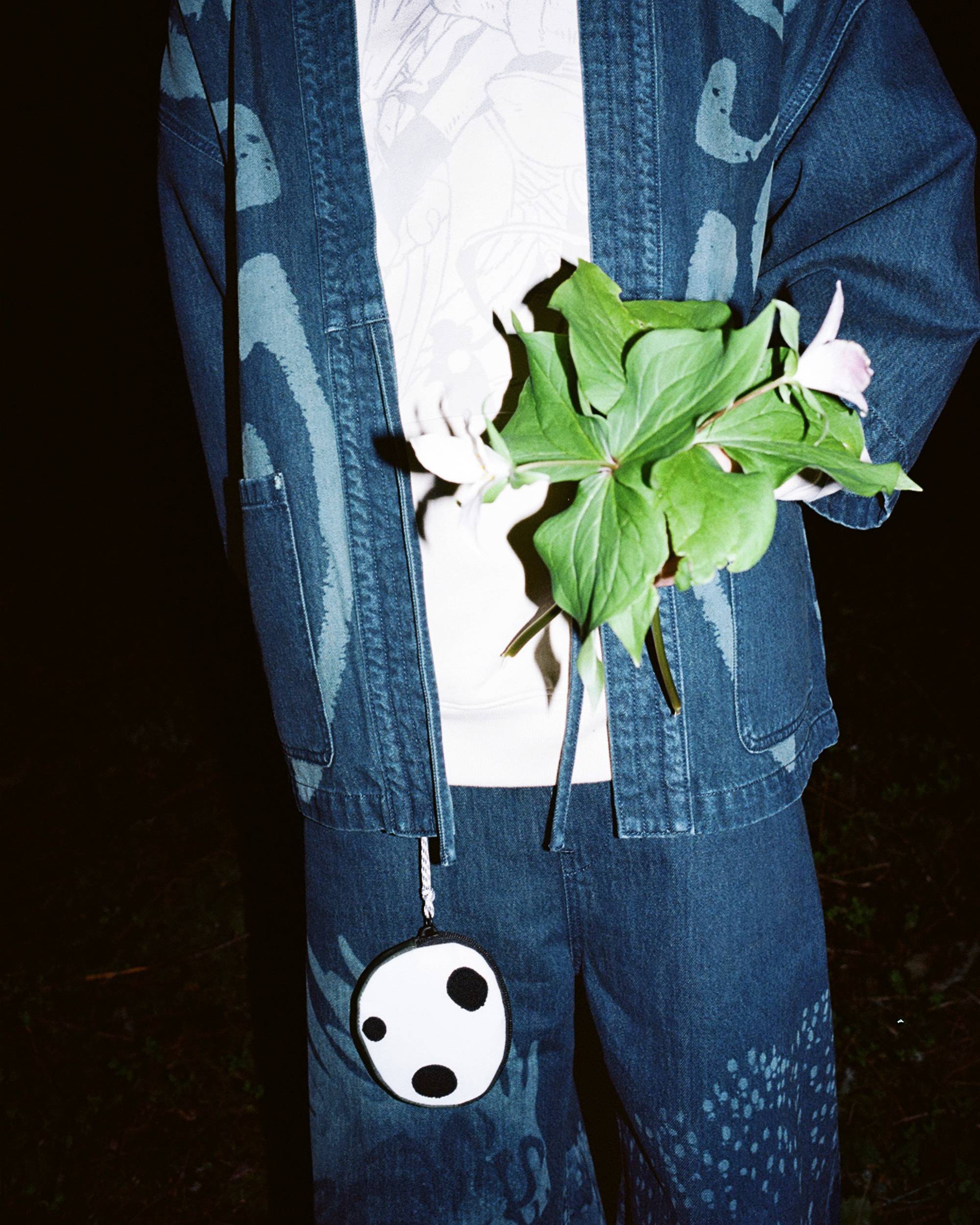 Image of person wearing Levi's® x Princess Mononoke collection pieces and posing with flower in nighttime forest setting