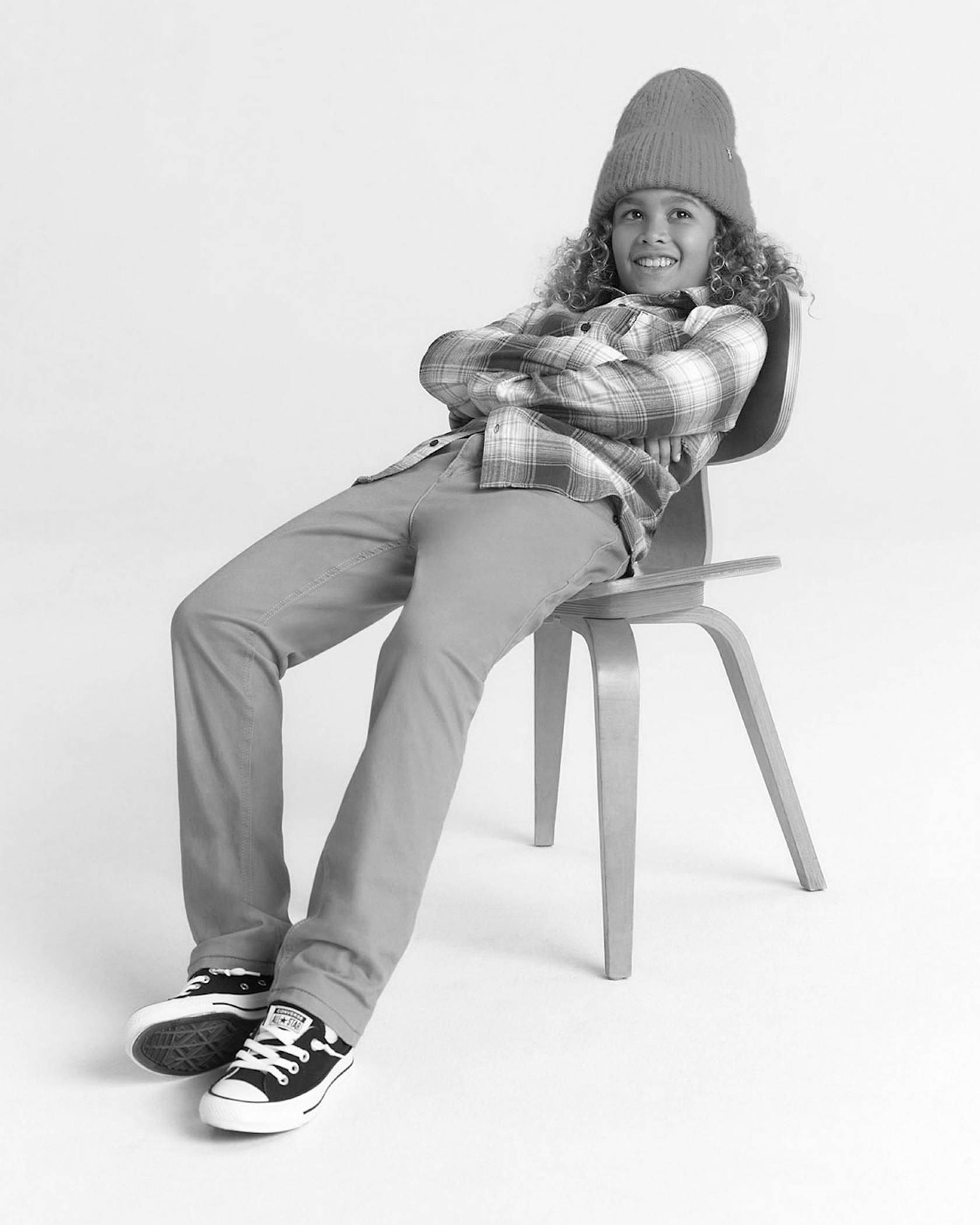 Black and white photo of model sitting in a chair wearing beanie, flannel shirt and jeans